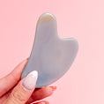 Load image into Gallery viewer, Fingers holding a soft-grey agate gua sha on a pale pink background.