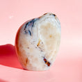 Load image into Gallery viewer, Soft white agate freeform with brown flower inclusions and black speckles throughout, set on a pale pink background.