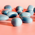 Load image into Gallery viewer, Multiple soft blue angelite tumble lay in the center of the image on an orange background with only the center stone in focus