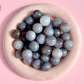 Load image into Gallery viewer, Group of grey agate spheres lay in a large fuzzy beige bowl on a pink background.