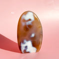 Load image into Gallery viewer, Dark brown-orange agate freeform with clusters of white inclusions on a pale pink background.