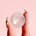 Load image into Gallery viewer, Fingers holding a pale white agate donut on a pale pink background. 
