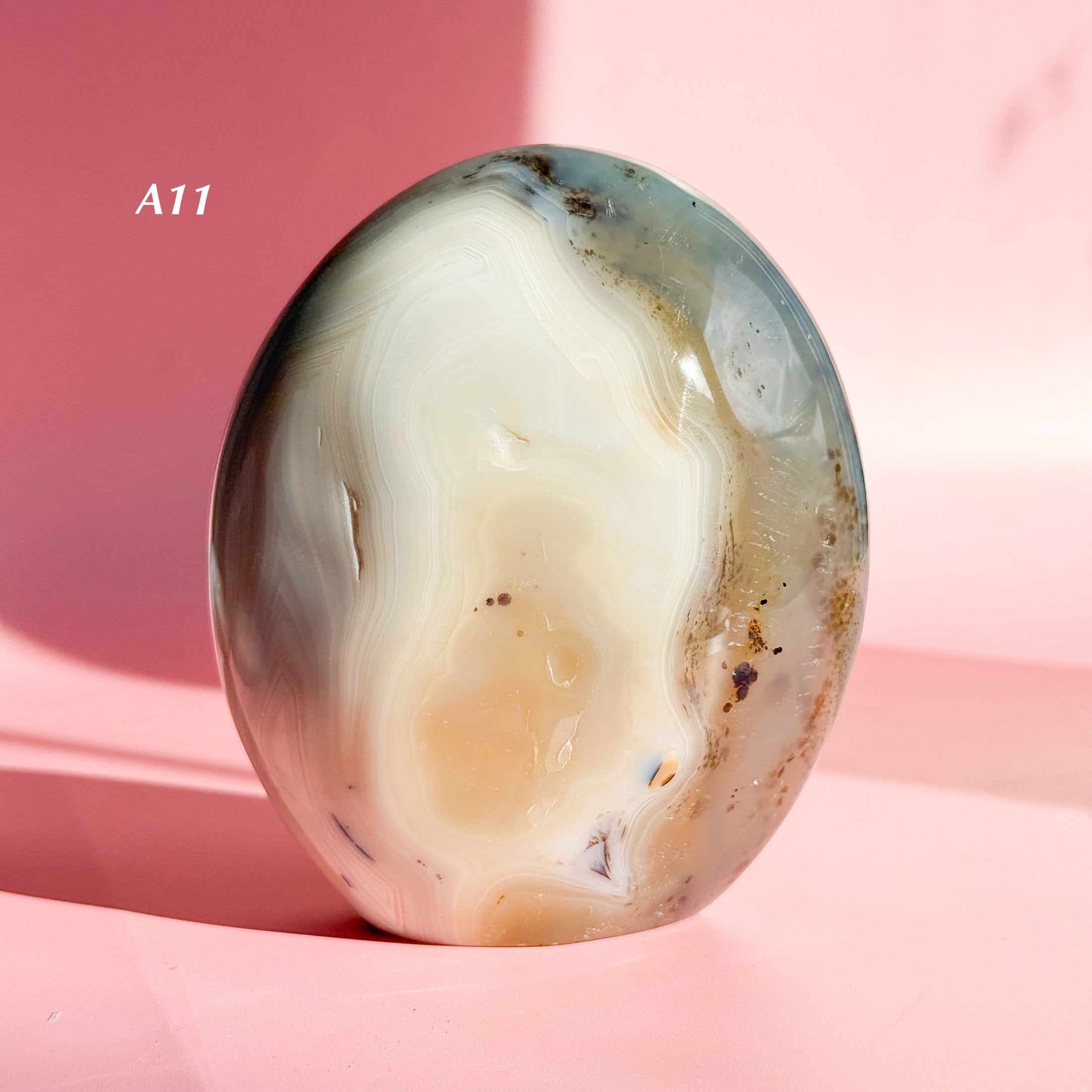 White and grey agate freeform with large white inclusion and black speckles throughout set on a soft pink background. 