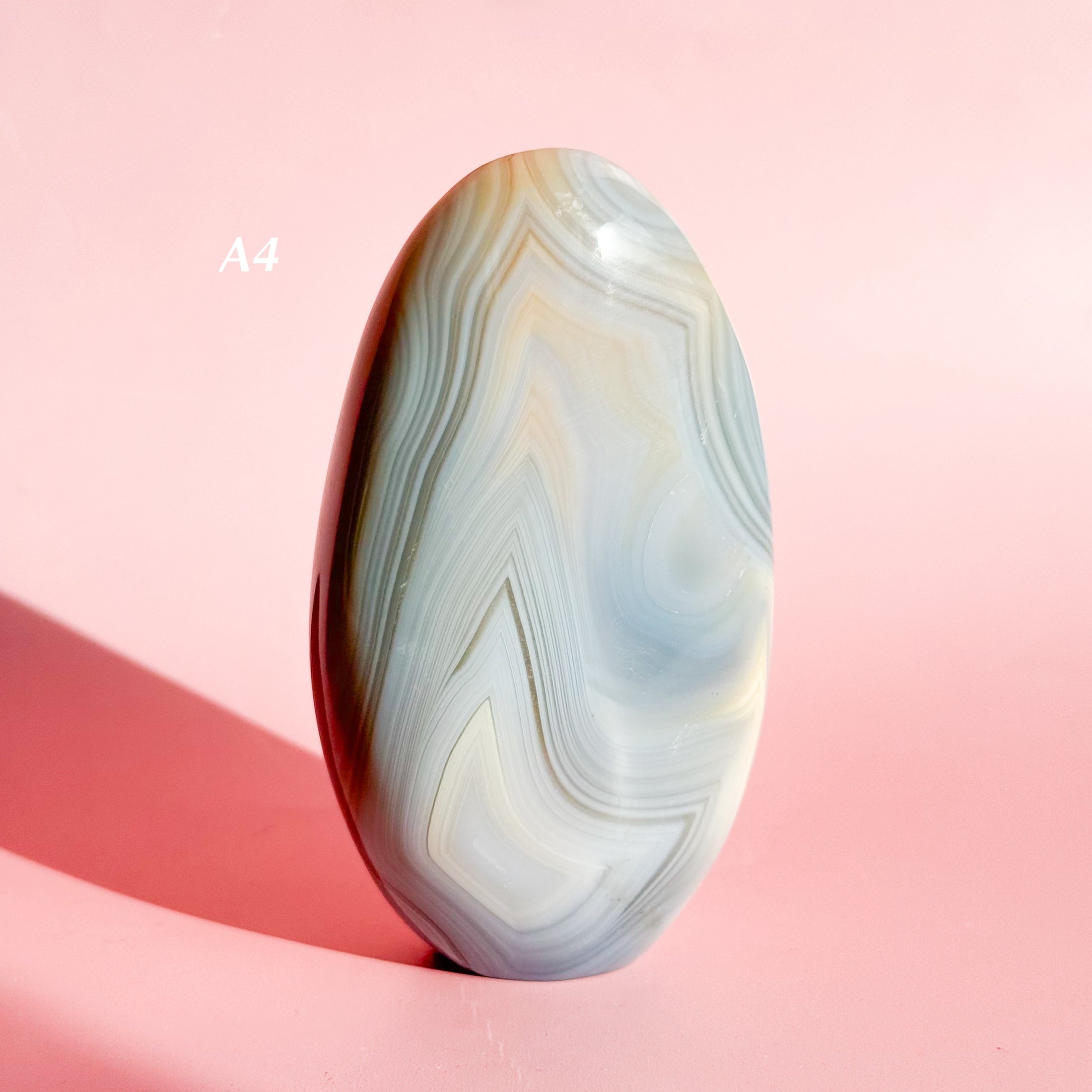 Soft gray agate freeform with many white and brown inclusions on a soft pink background. 