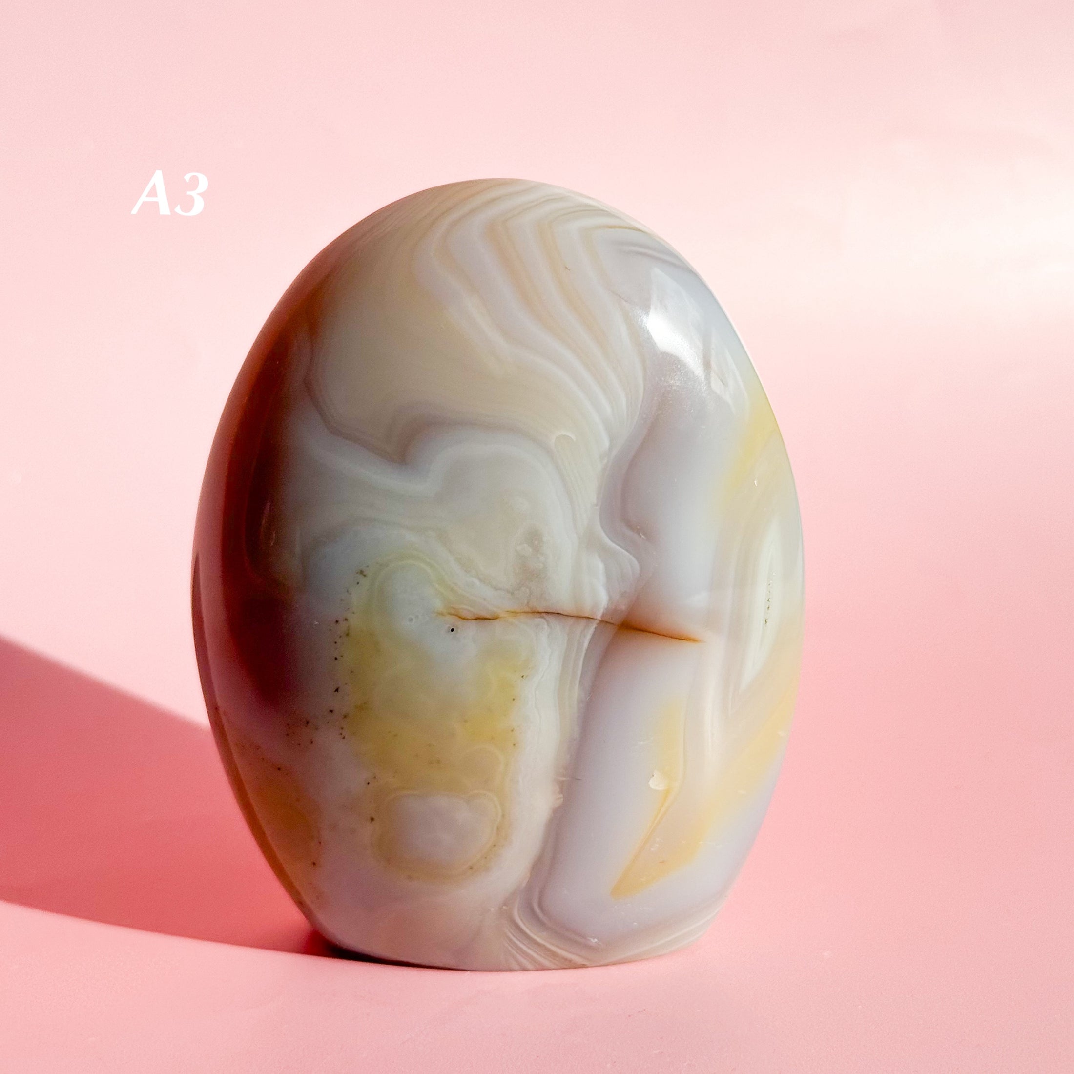 Pale grayish-pink agate freeform with yellow and white inclusions set on a soft pink background. 