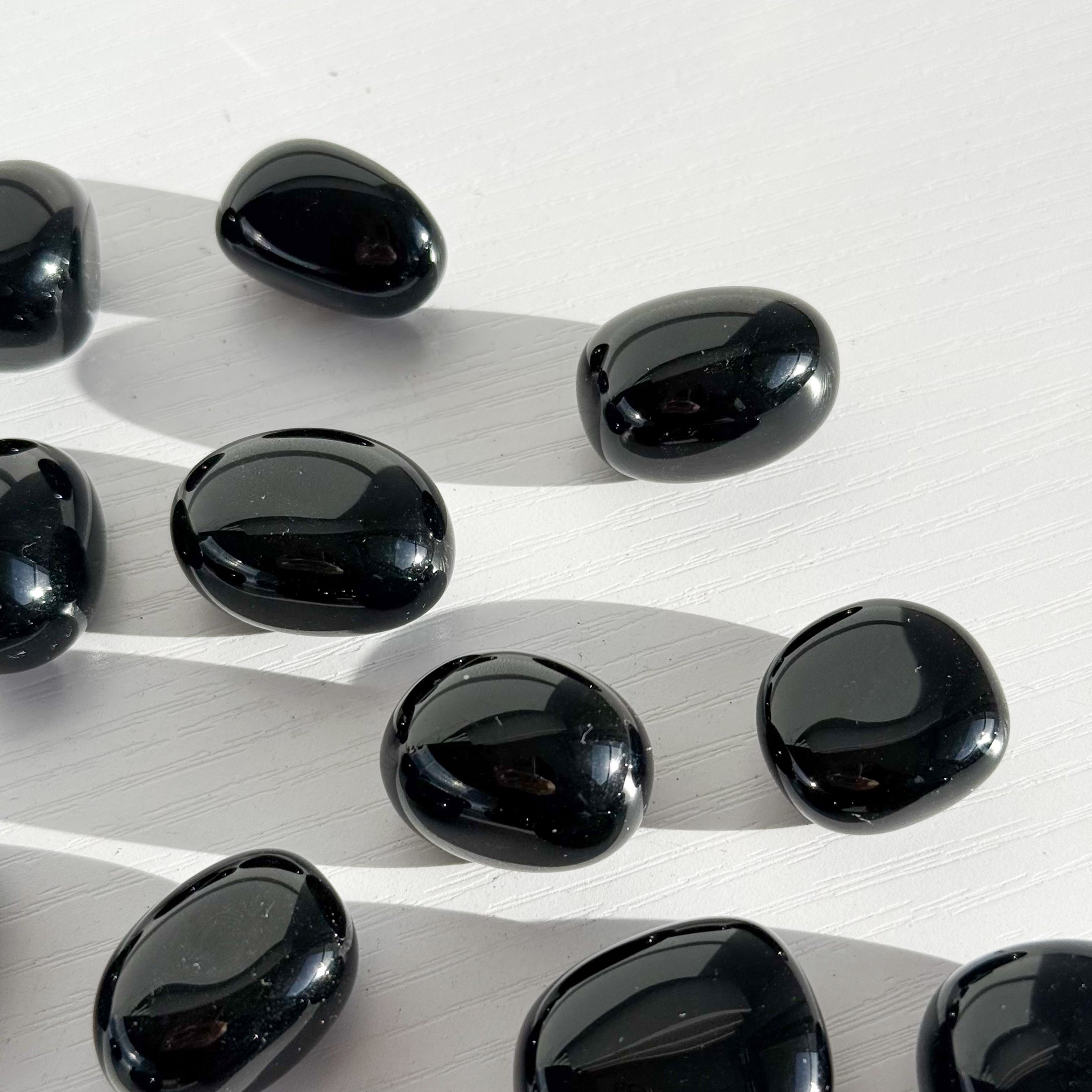 Group of black obsidian tumbles lay scattered in the center of the image on a white background. 