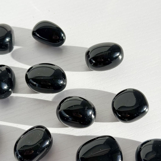Group of black obsidian tumbles lay scattered in the center of the image on a white background. 