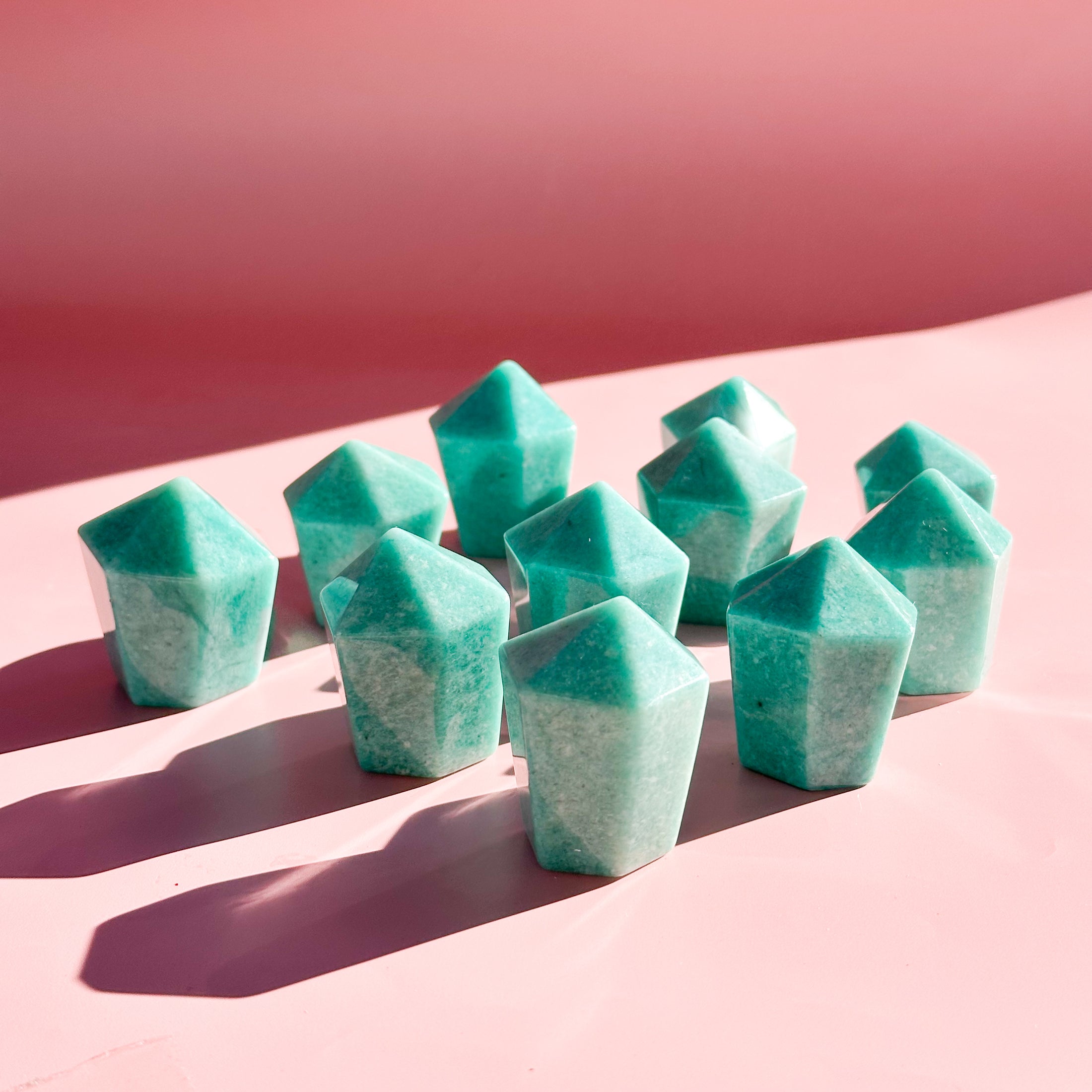 Eleven teal amazonite towers stand in the center of the image with pale pink foreground and darker pink background. 