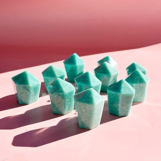 Eleven teal amazonite towers stand in the center of the image with pale pink foreground and darker pink background. 