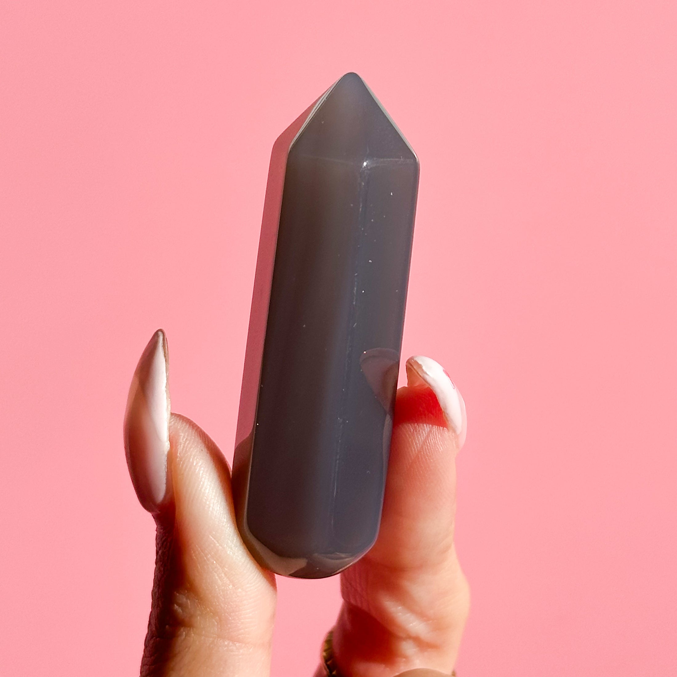 Fingers hold dark grey agate point set on a soft pink background. 