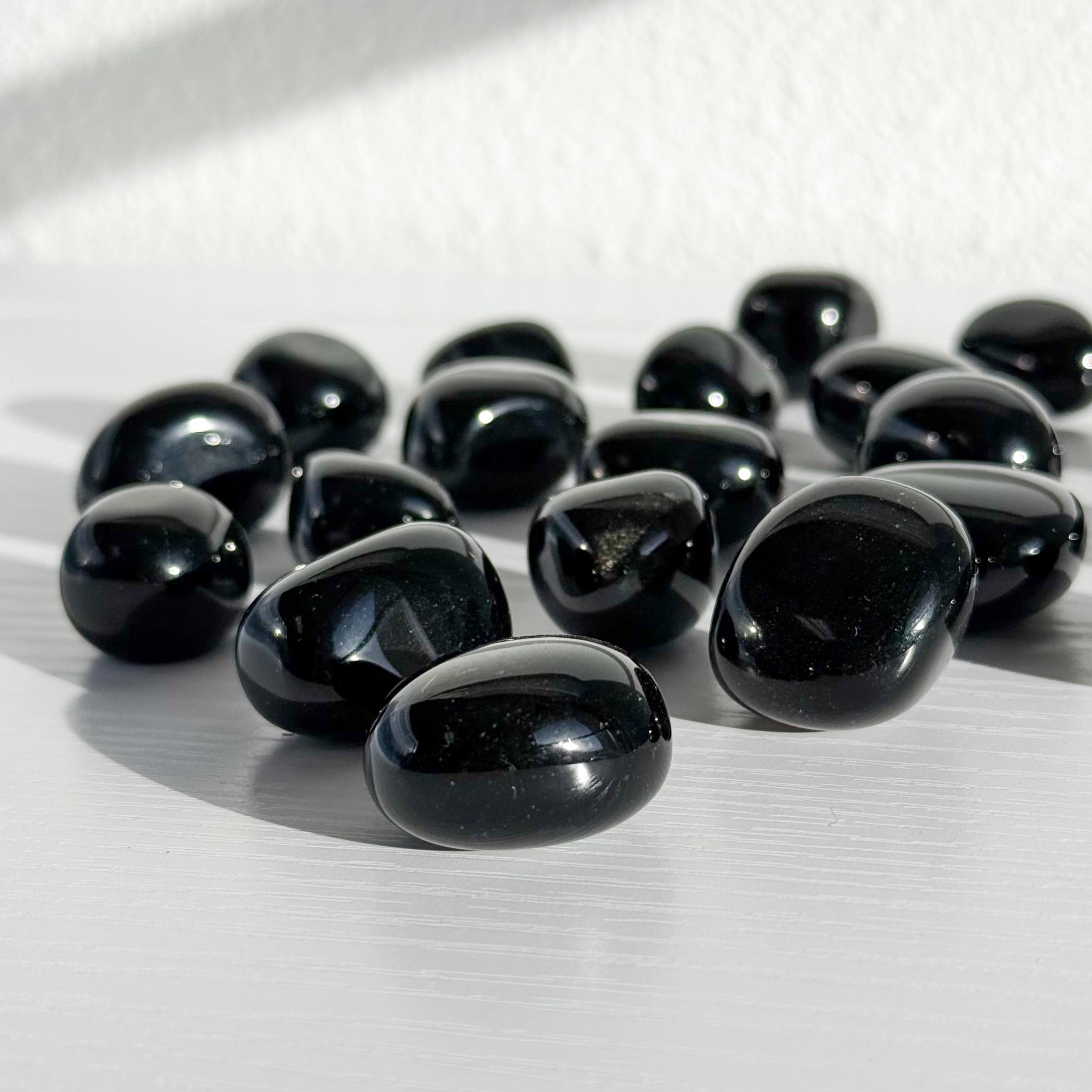 Group of black obsidian tumbles lay scattered in the center of the image on a white background. 