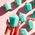 Load image into Gallery viewer, Hand holds teal amazonite tower with eight out-of-focus towers in the background set on a pale pink background. 
