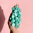 Load image into Gallery viewer, Hand holds a pile of teal amazonite flat stones on a soft pink background. 
