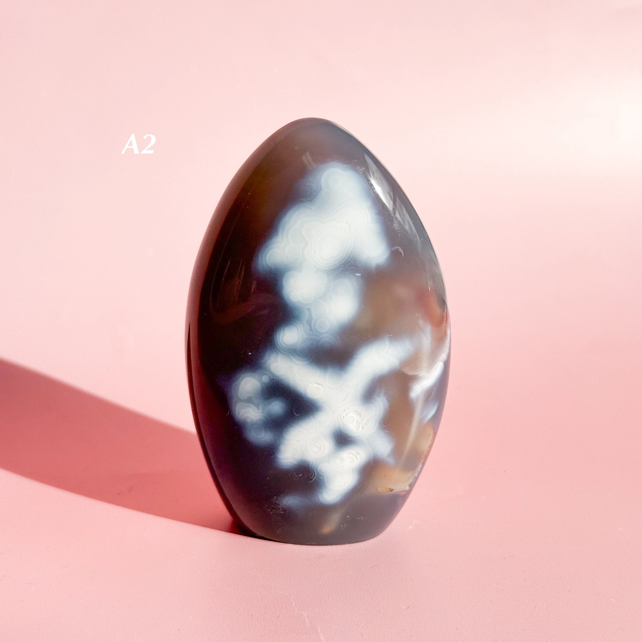 Dark grey agate freeform with groups of white inclusions set on a soft pink background. 