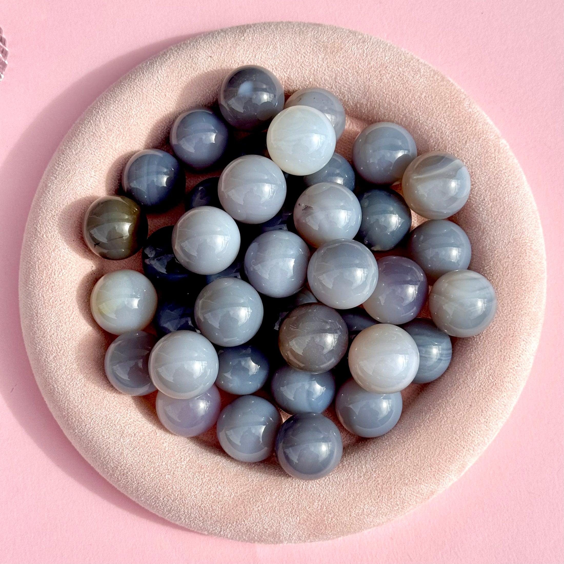 Group of grey agate spheres lay in a large fuzzy beige bowl on a pink background. 