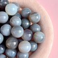 Load image into Gallery viewer, Zoomed in shot of grey agate spheres in a beige fuzzy bowl in the left portion of the image on a pink background. 
