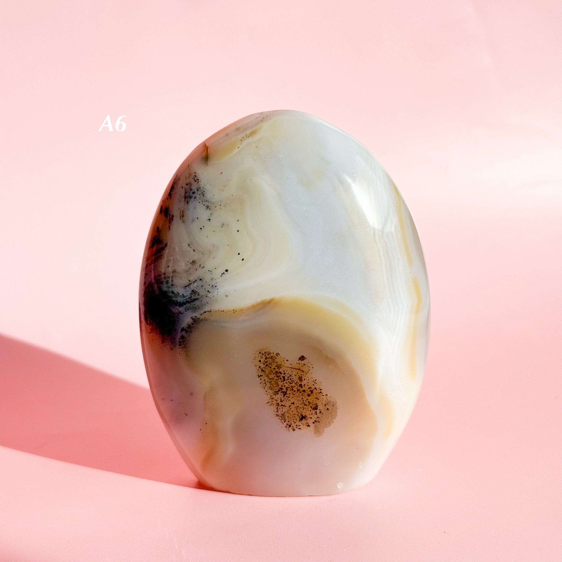 Pale grey and brown agate freeform with black speckles throughout, set on a pink background. 