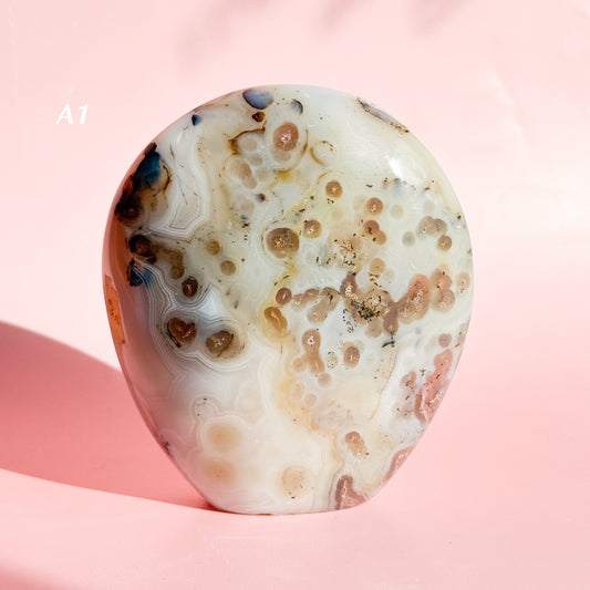 White agate freeform with pale brown spots throughout the stone set on a pink background. 
