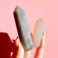 Load image into Gallery viewer, Hand holds two agate points, one grey and one beige on a soft pink background. 
