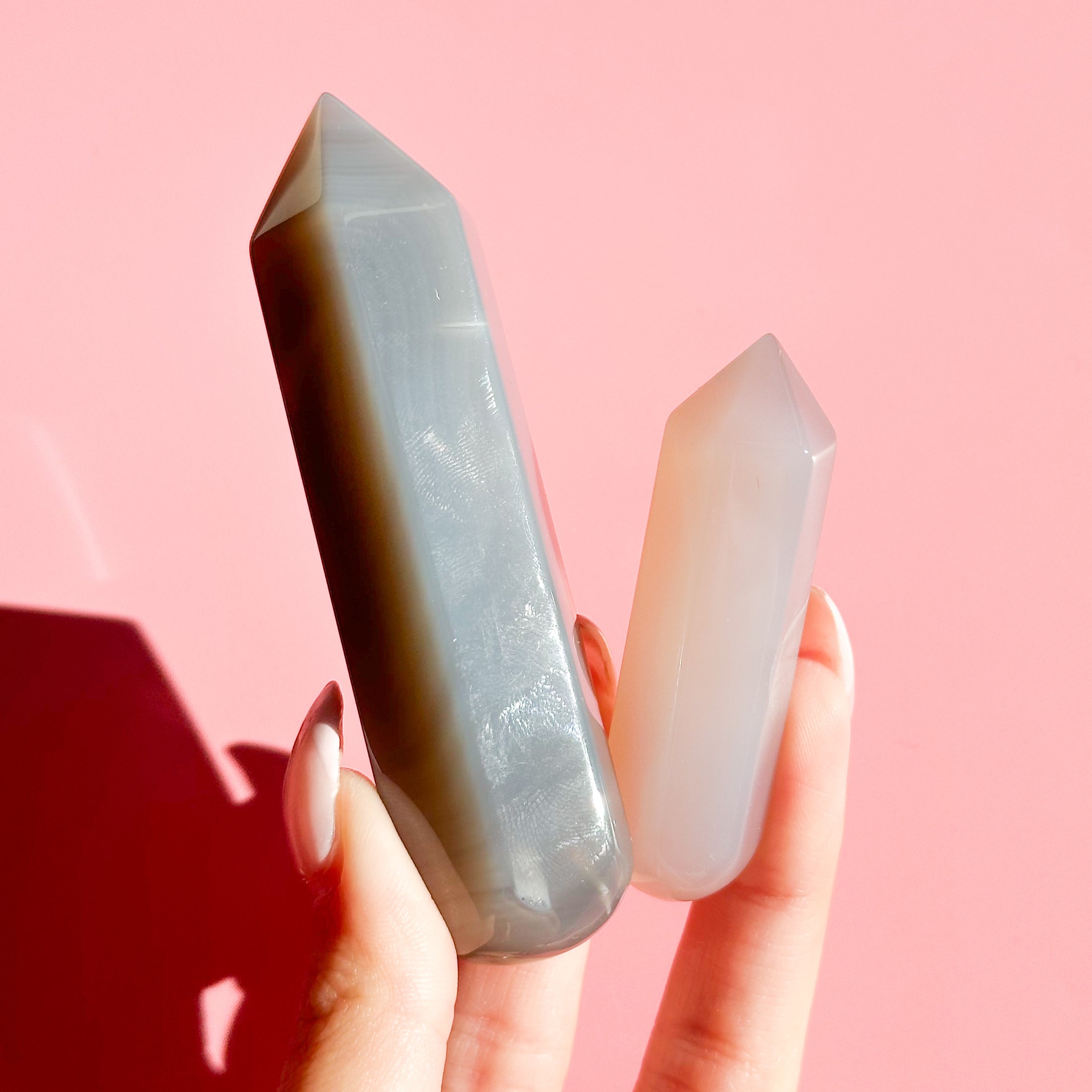 Hand holds two agate points, one grey and one beige on a soft pink background. 