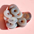 Load image into Gallery viewer, Pile of pale grey agate donuts in a pink heart bowl on a soft pink background.  
