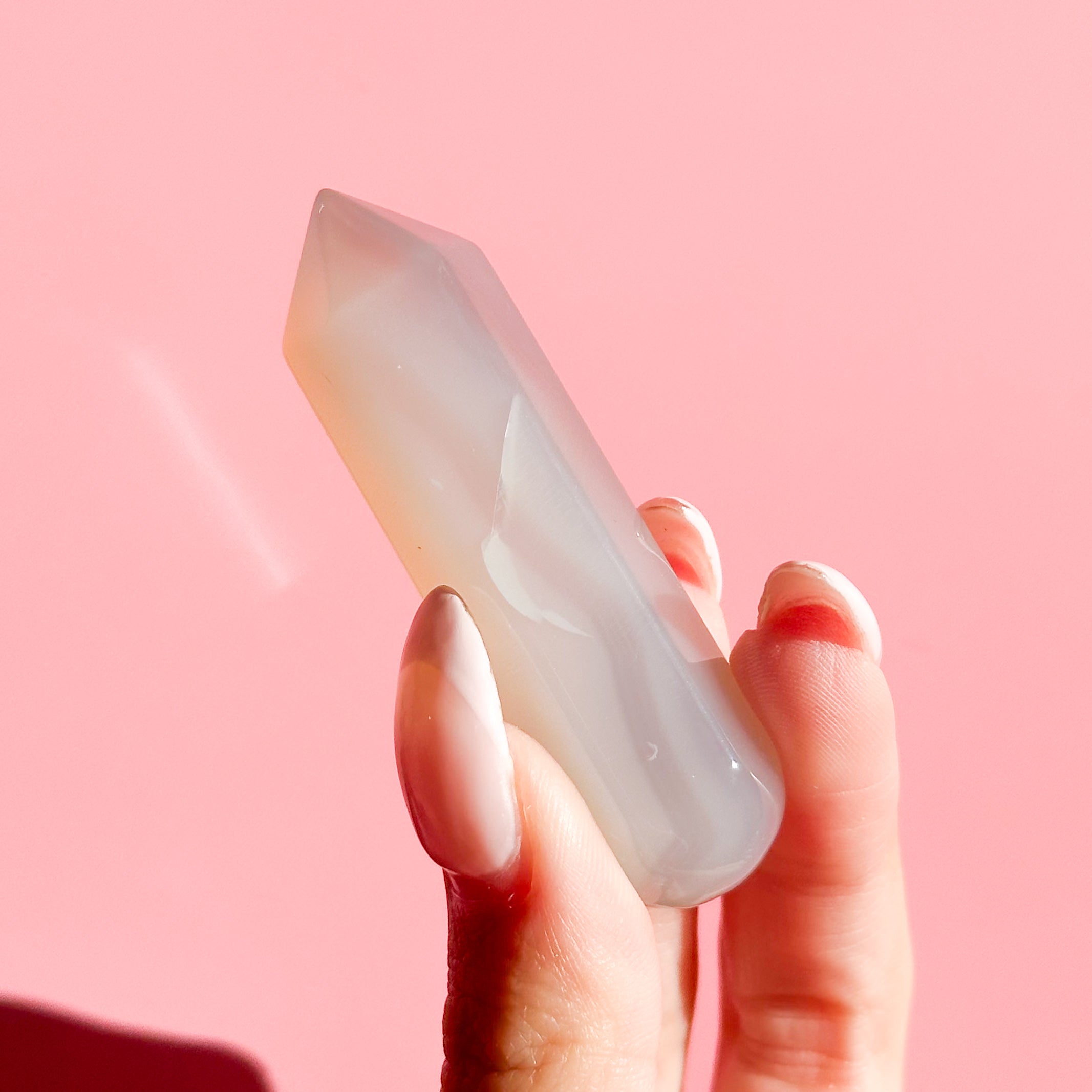 Hand holds pale white agate point on a soft pink background. 