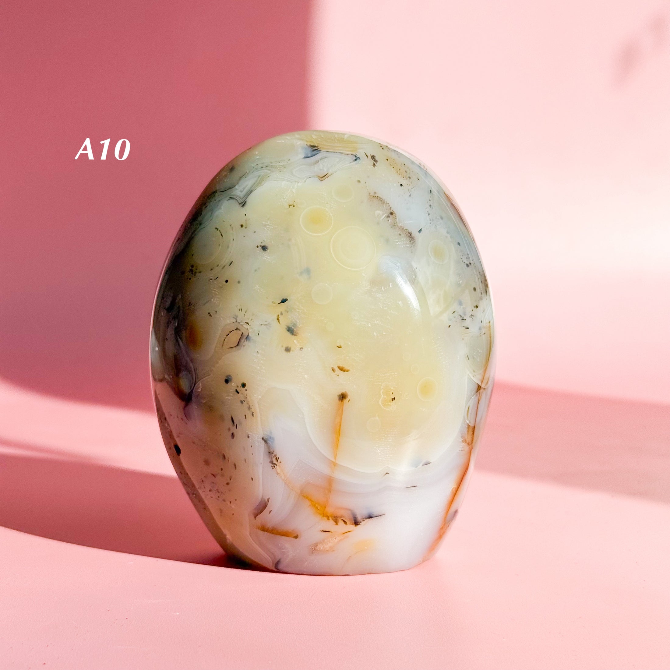 Ivory agate freeform with black speckles and white inclusions set on a soft pink background. 