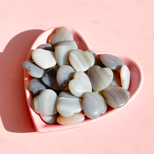 Group of grey and white agate hearts lay in a pink heart bowl on a soft pink background. 