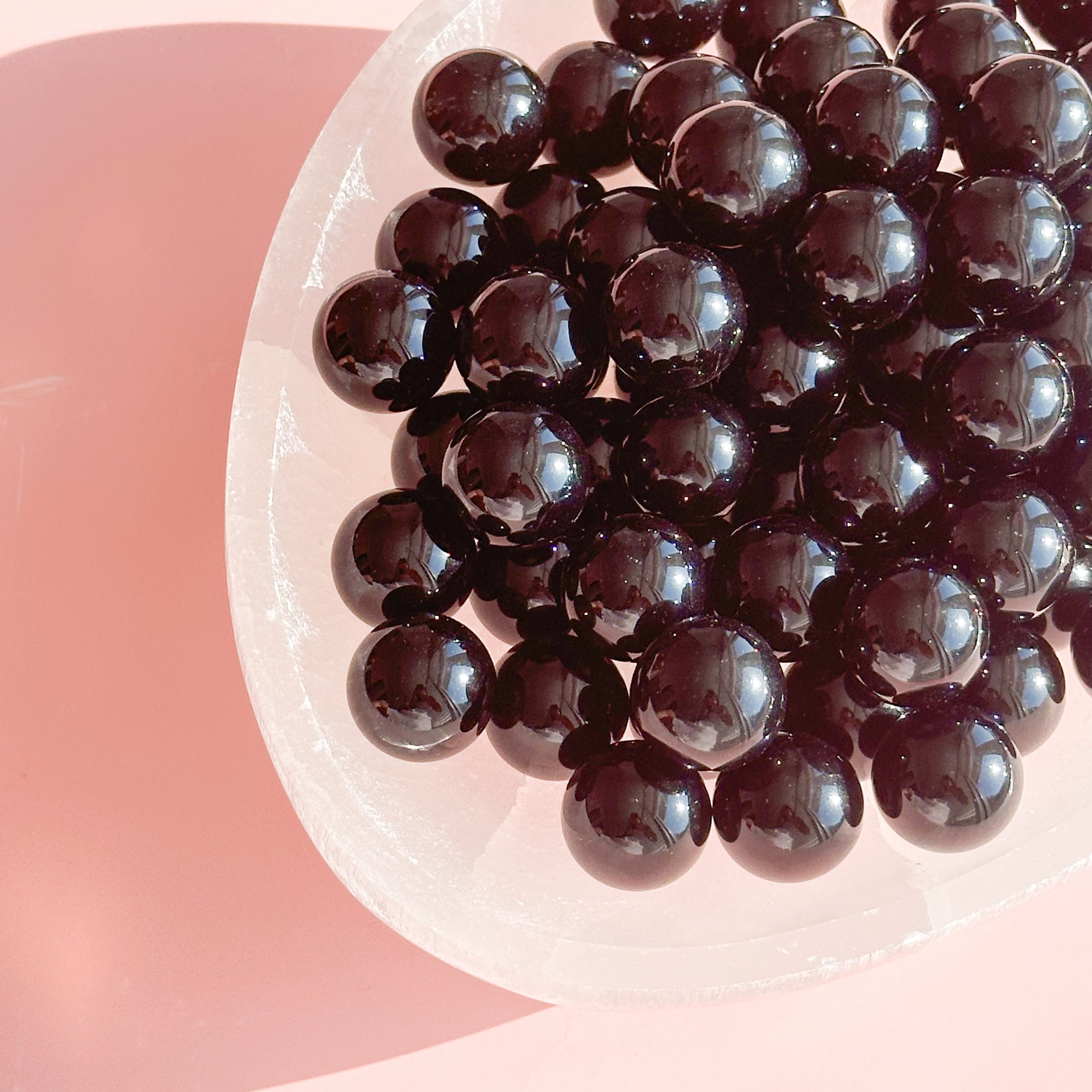 A large white bowl sits in the top right corner of the image, full of black obsidian spheres. 