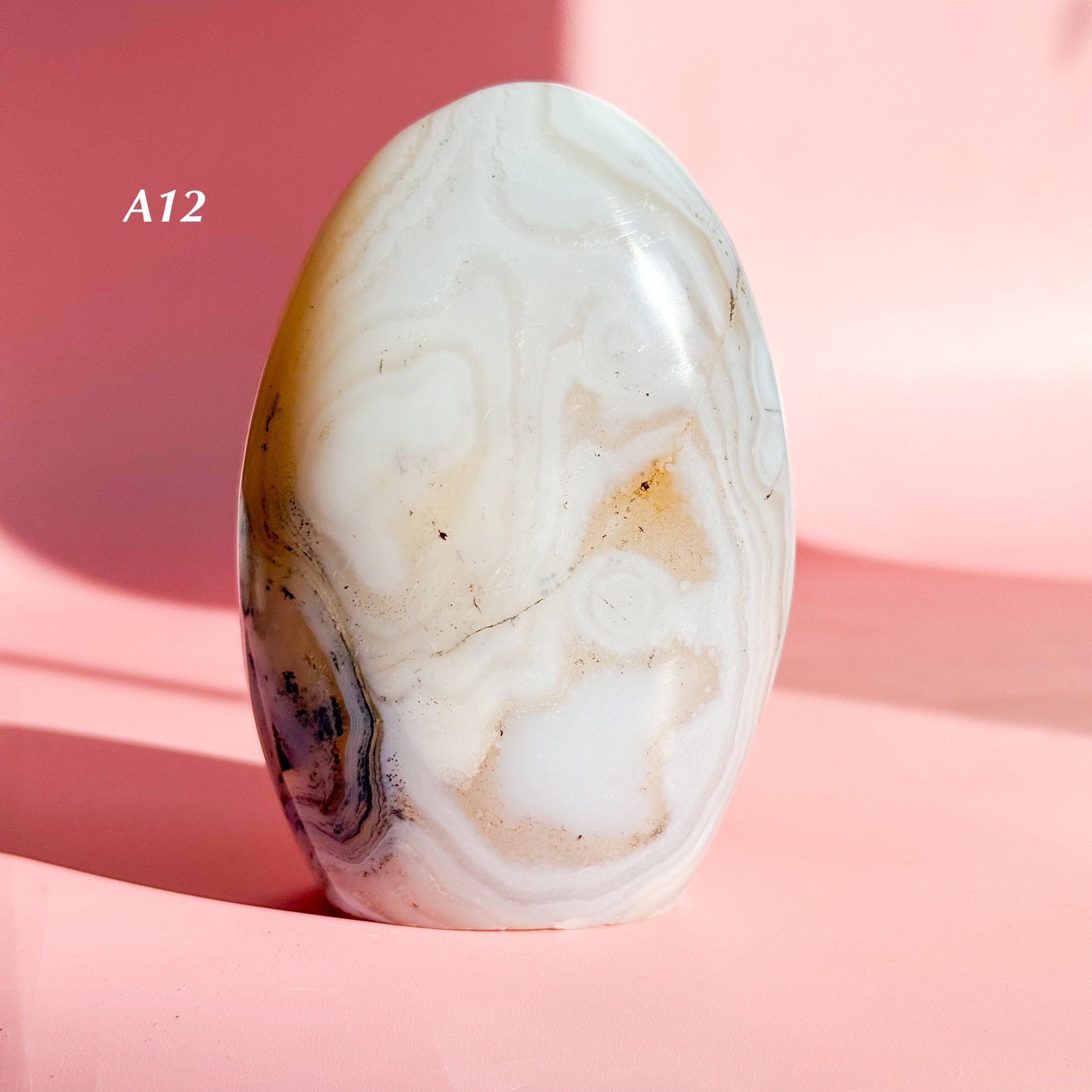 White agate freeform with light brown and black glitter speckles set on a soft pink background. 