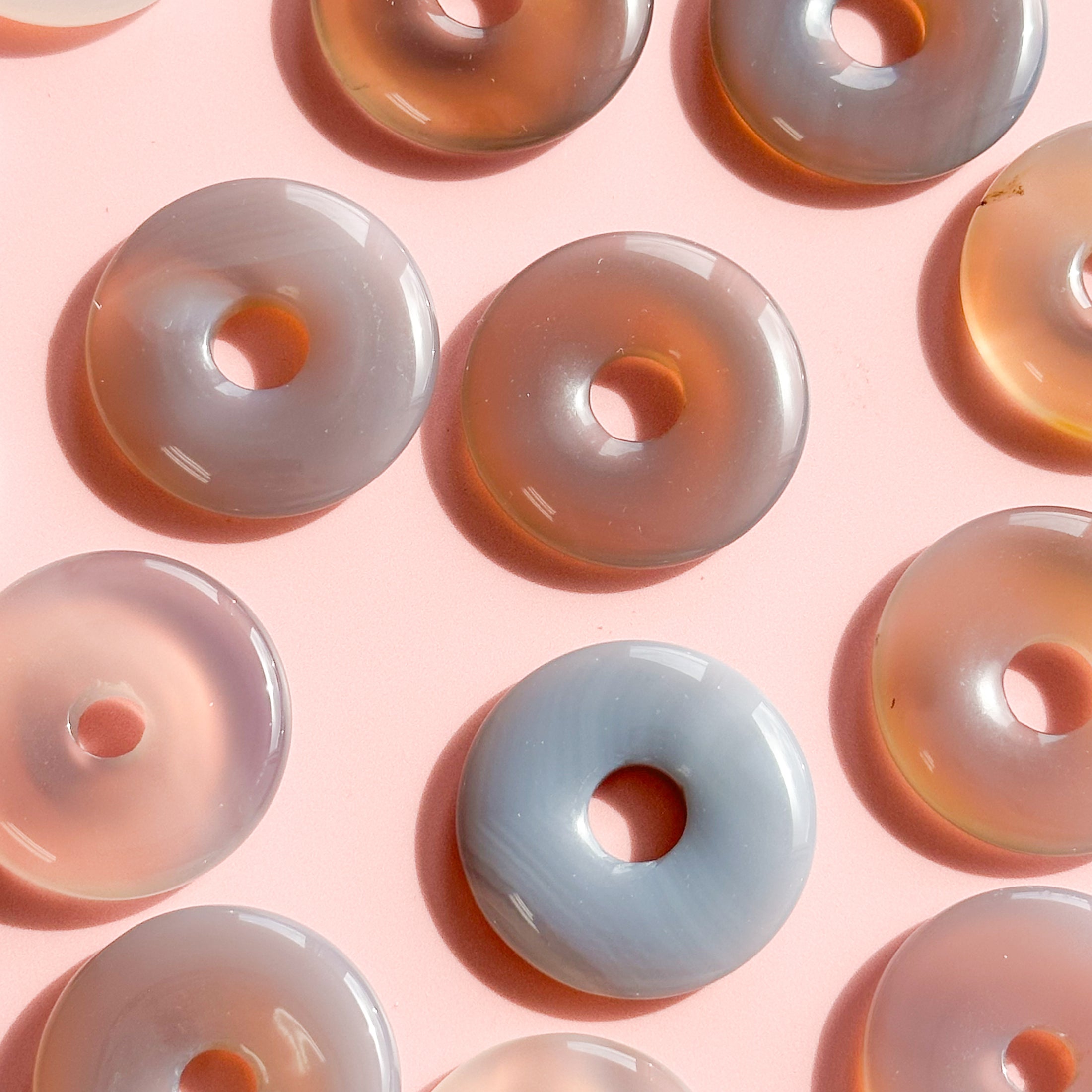 10 grey and brown agate donuts laid flat and arranged on a pale pink background
