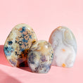 Load image into Gallery viewer, Group of three agate free forms with the two tallest in the back and the shortest in the front set on a soft pink background. 
