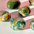 Load image into Gallery viewer, Six green, yellow, and blue bloodstone tumbles lie scattered in the center of the screen on a soft pink background. 
